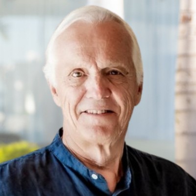 A smiling older man with white hair wearing a dark blue shirt, set against a soft blurred background.